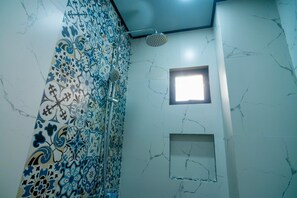 Un baño con ducha, una ventana pequeña y azulejos decorativos.