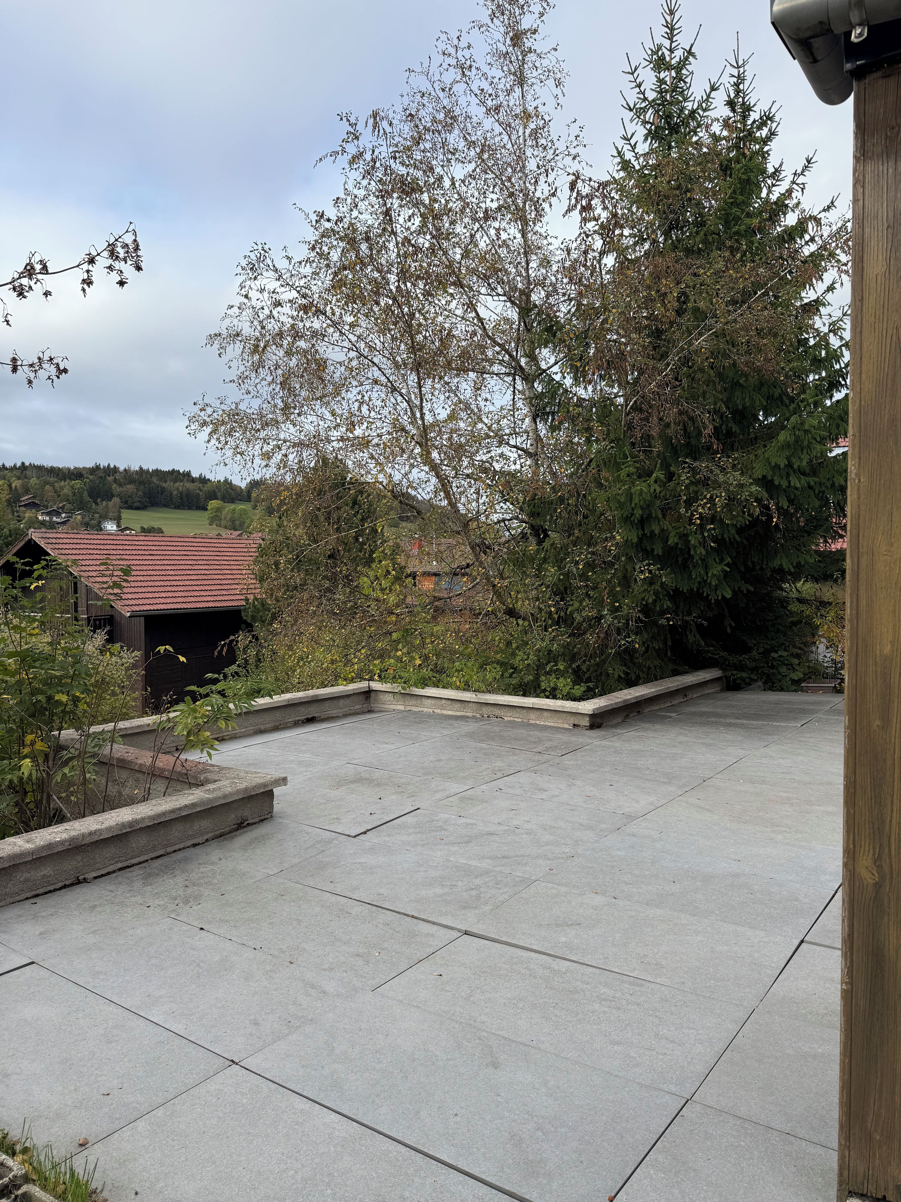 Une terrasse sur le toit offrant une vue sur une colline boisée, un petit bâtiment avec un toit rouge et une structure en bois sur la droite.