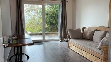 A room with a wooden ceiling, a sliding glass door leading to an outdoor area, a sofa, and a small table with a kettle.