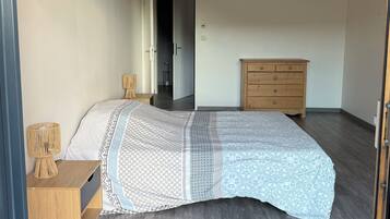 A bedroom with a bed, a wooden dresser, a nightstand, and a door leading to another room.