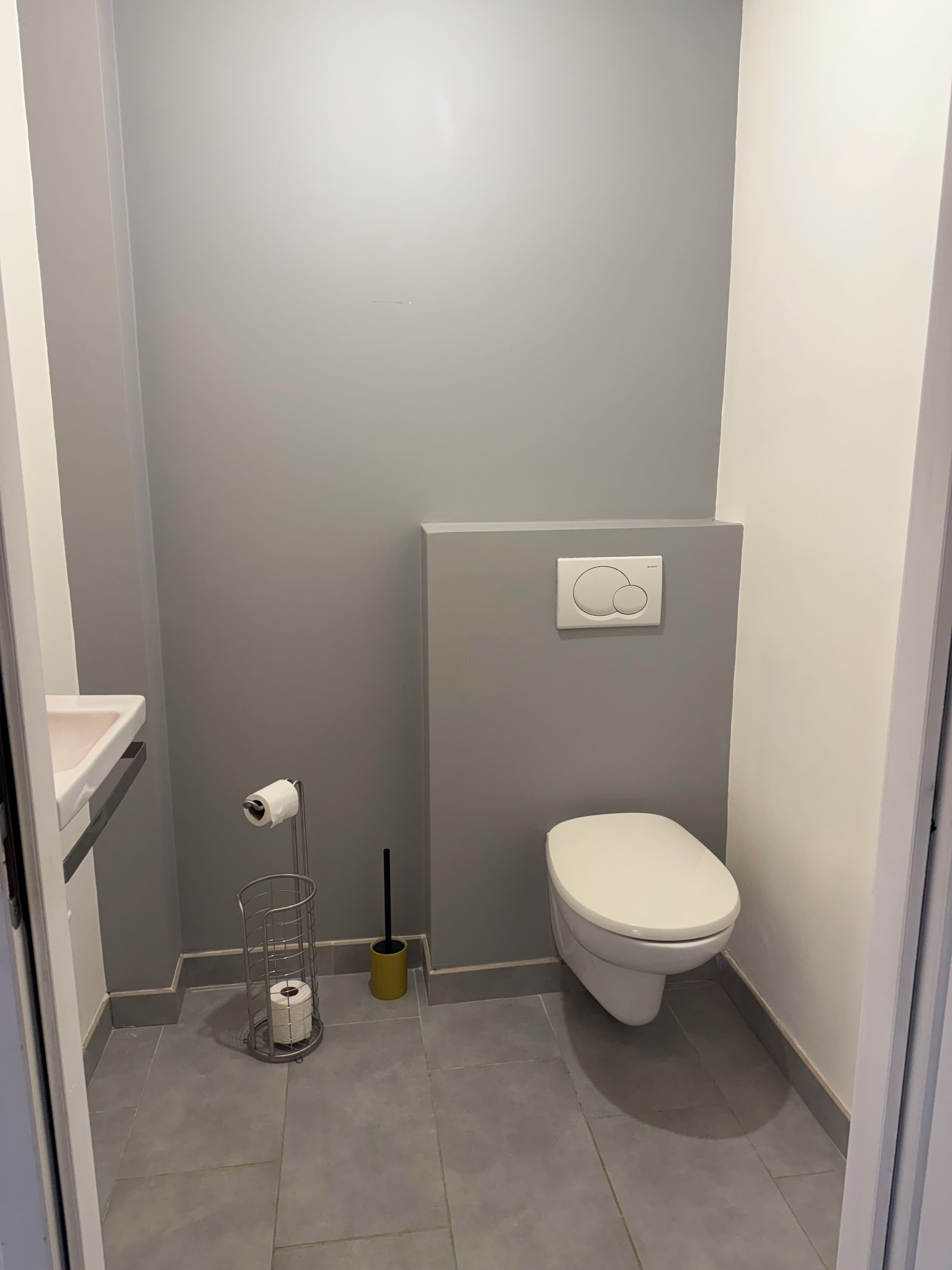 A small, clean bathroom with a toilet, a toilet paper holder, and a plunger on the floor.