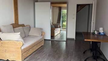 A room with a wooden ceiling, a wooden sofa, a dining table, and a view through a glass door.