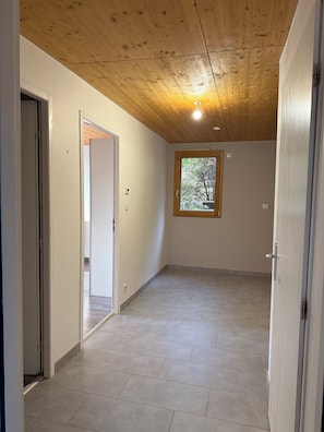 A room with a wooden ceiling, a window with a view of trees, and a tiled floor.