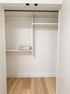 A white closet with a shelf and hanging space, wooden flooring, and a white wall. - Ladner suite, kitchen, A/C and laundry (Delta)