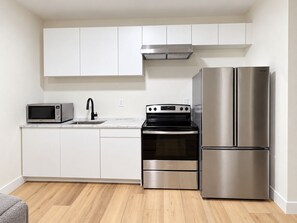 A modern kitchen with white cabinets, a stainless steel refrigerator, a microwave, and a stove. - Ladner suite, kitchen, A/C and laundry (Delta)