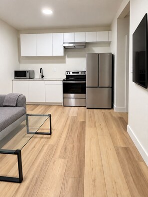 A modern kitchen with white cabinets, a stainless steel oven, a microwave, and a refrigerator. - Ladner suite, kitchen, A/C and laundry (Delta)