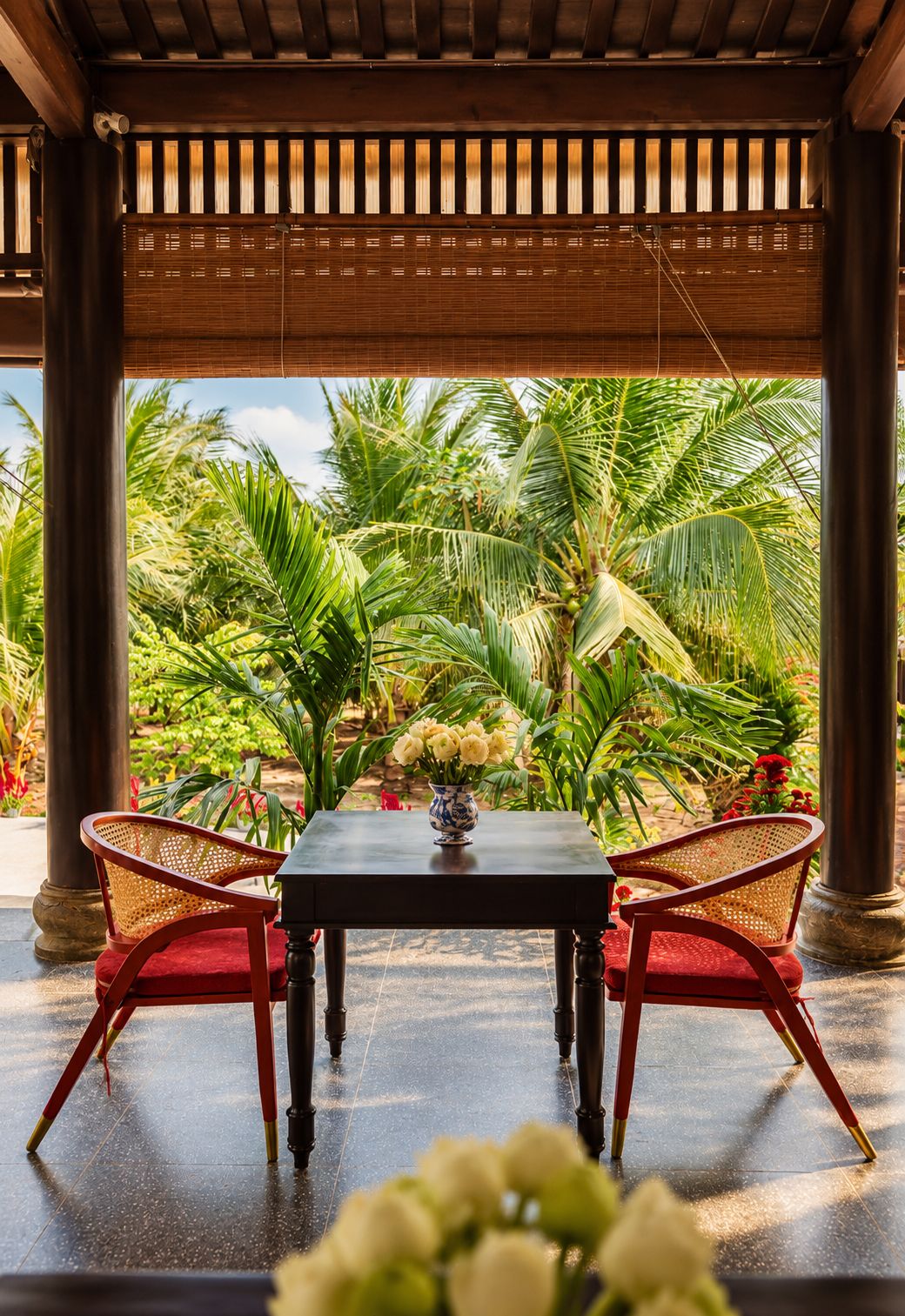 An outdoor seating area with a table and chairs, surrounded by lush greenery and palm trees.