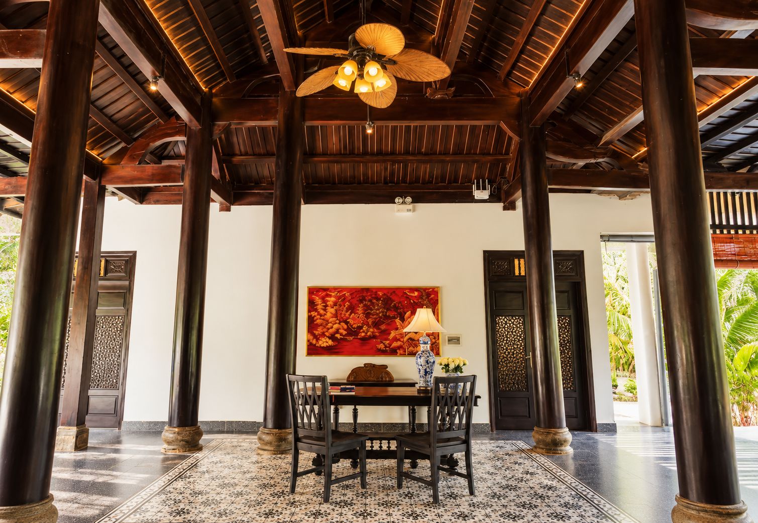 Área externa coberta com teto de madeira, mesa com cadeiras e um quadro na parede.