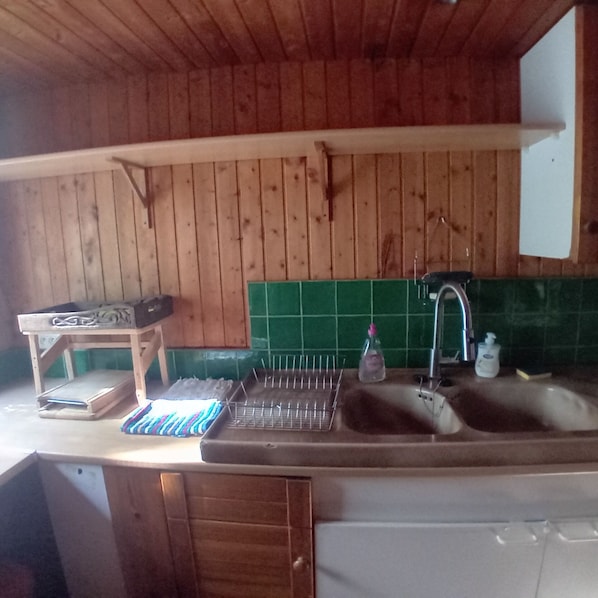 Una cocina con paredes de madera, un salpicadero de azulejos verdes, un lavamanos, un grifo, un dispensador de jabón y un perchero para toallas.