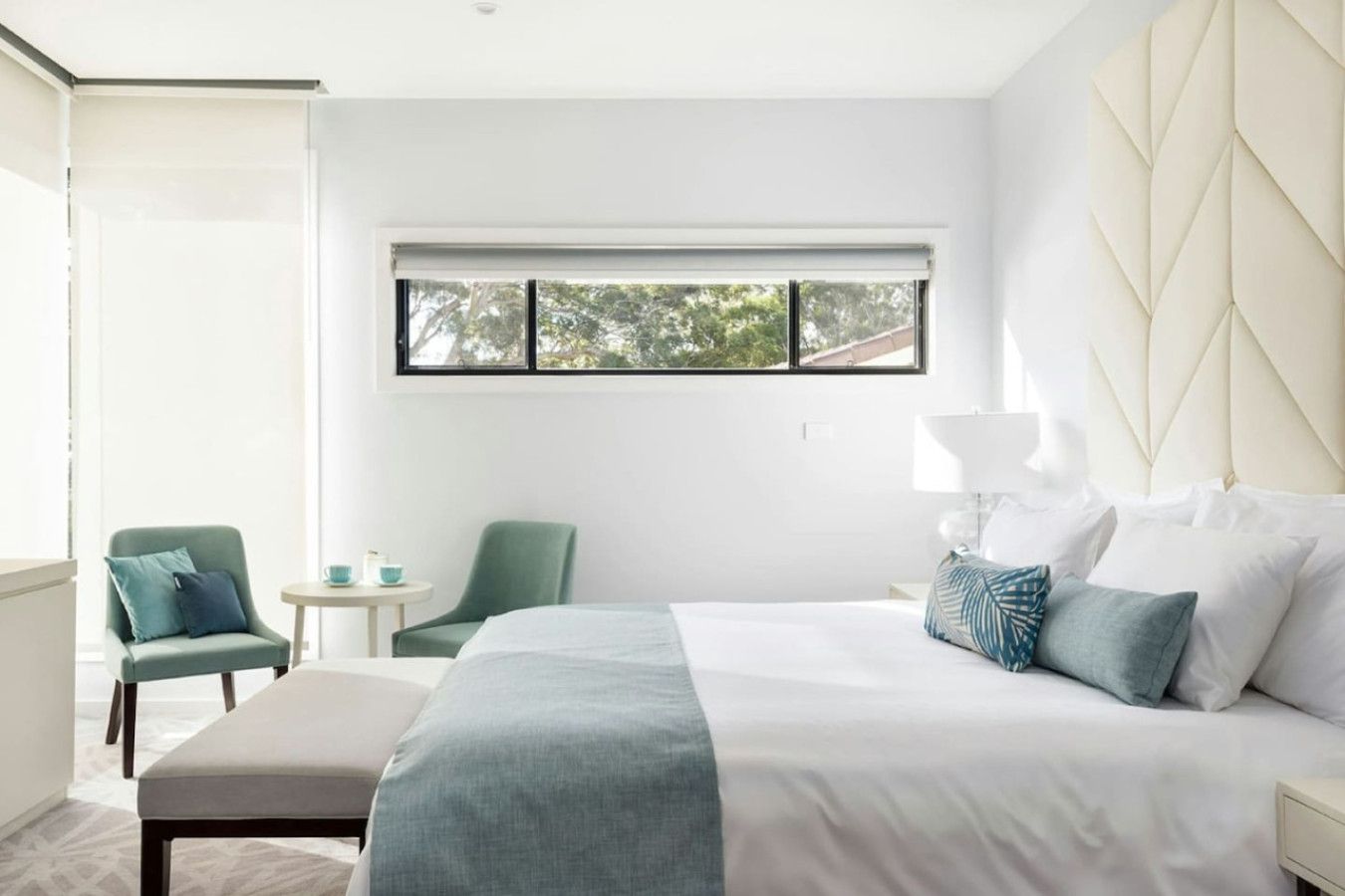 Un dormitorio moderno con una cama grande, una mesita, dos sillas y una ventana con vistas a árboles.
