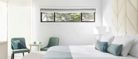 Un dormitorio moderno con una cama grande, una mesita, dos sillas y una ventana con vistas a árboles.