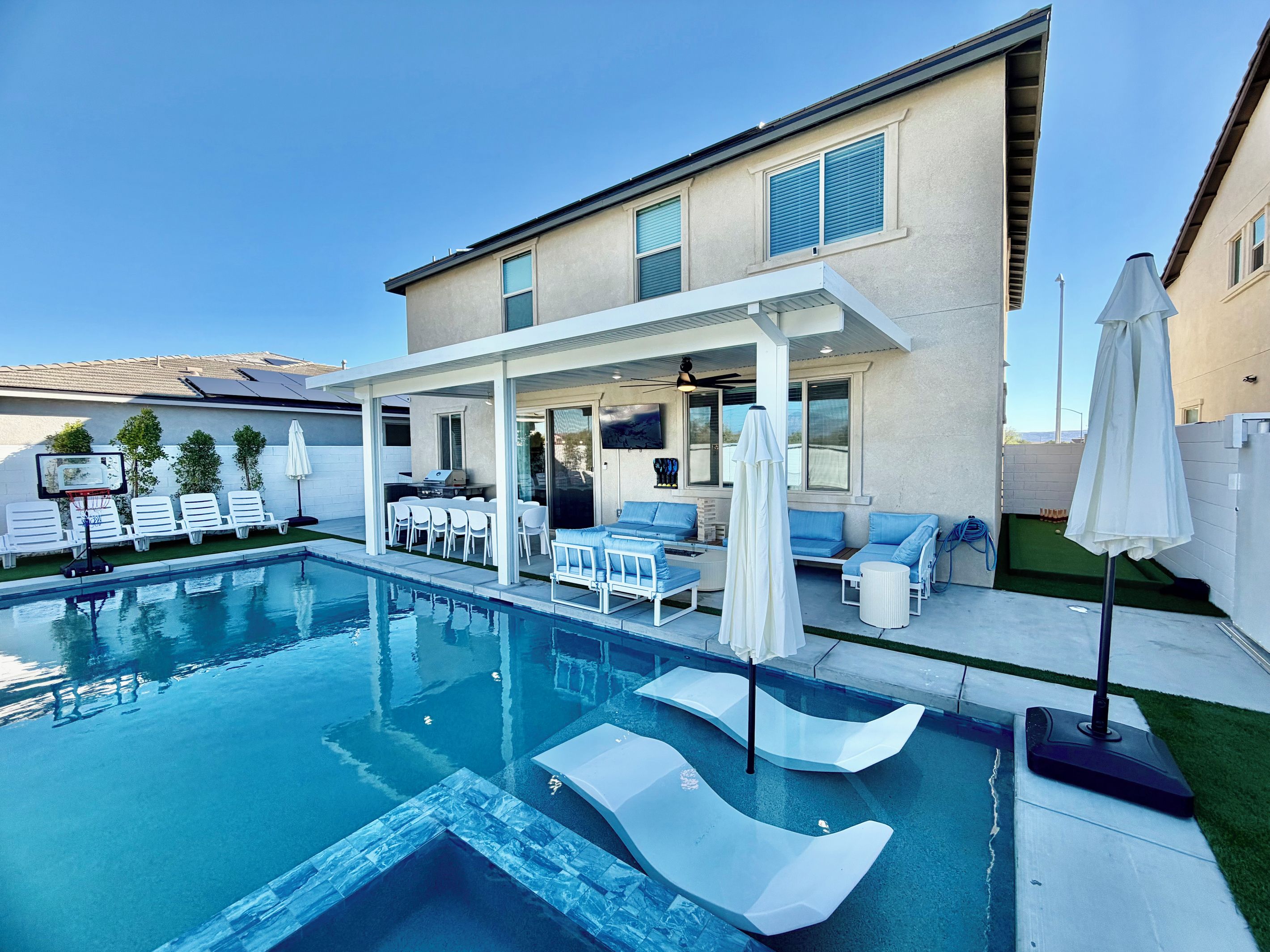 A modern outdoor pool area with lounge chairs, a barbecue, and a covered patio.
