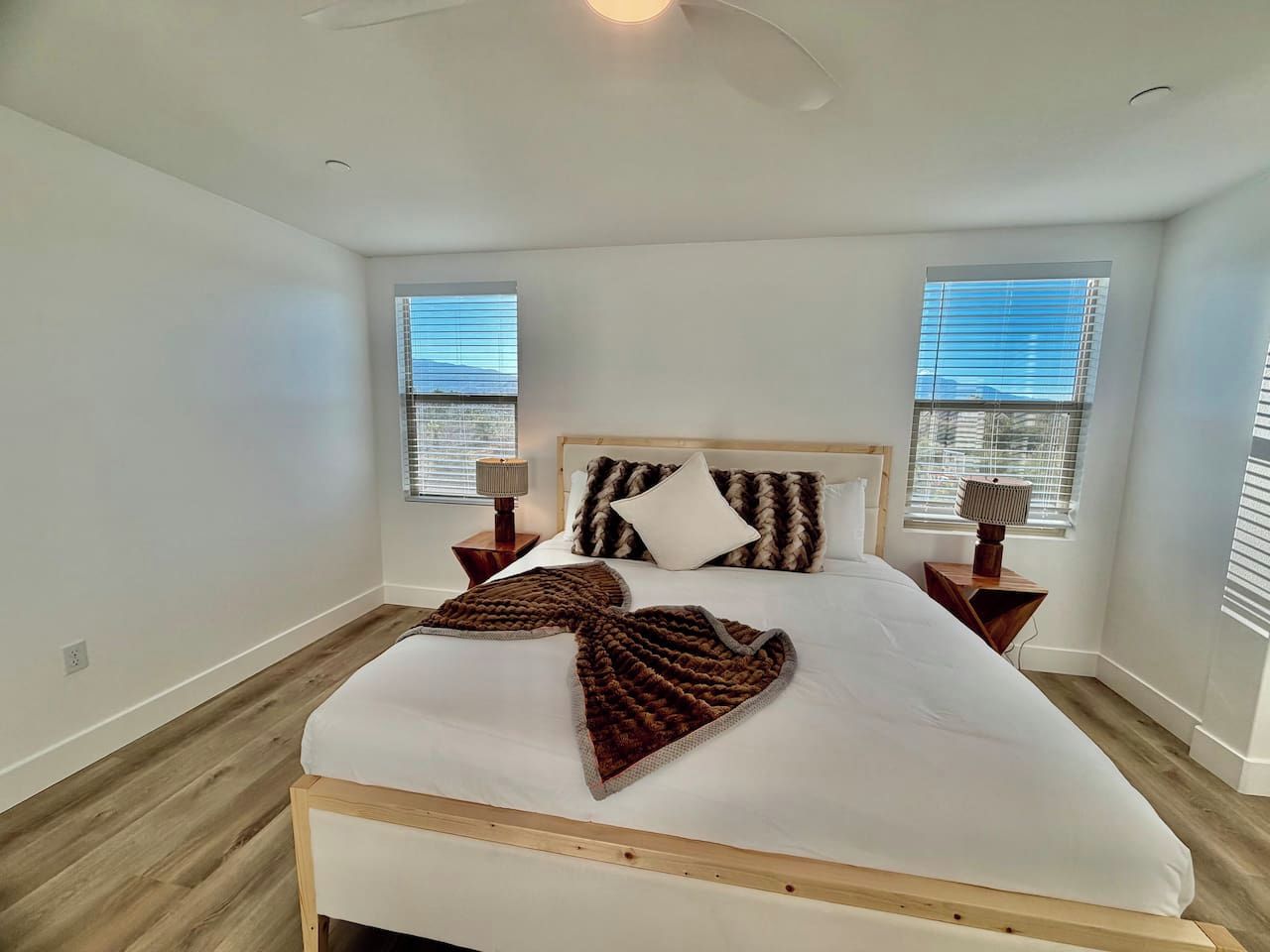 A bedroom with a bed, two bedside lamps, and a window with blinds.