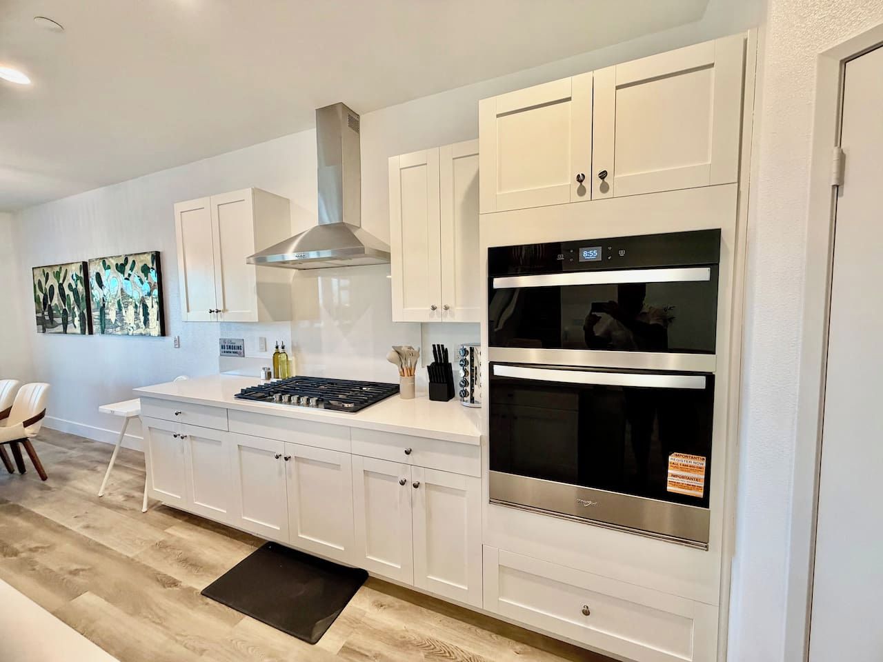 A modern kitchen with white cabinetry, a stainless steel range hood, a built-in oven, and a black countertop.