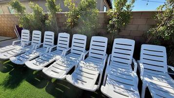 A row of white lounge chairs aligned on a green surface, likely a lawn, with a building in the background.