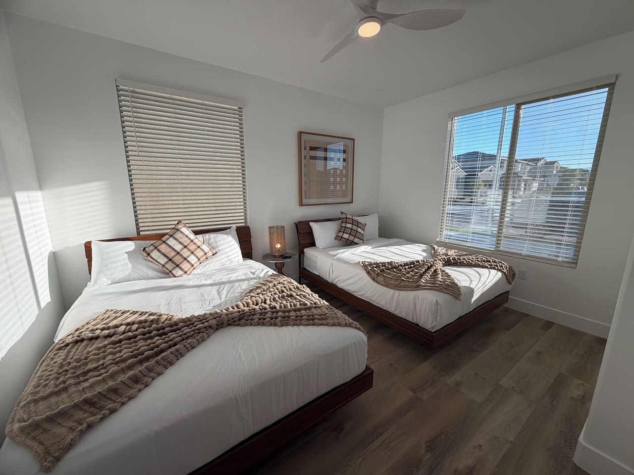 A bedroom with two beds, a ceiling fan, and a large window.