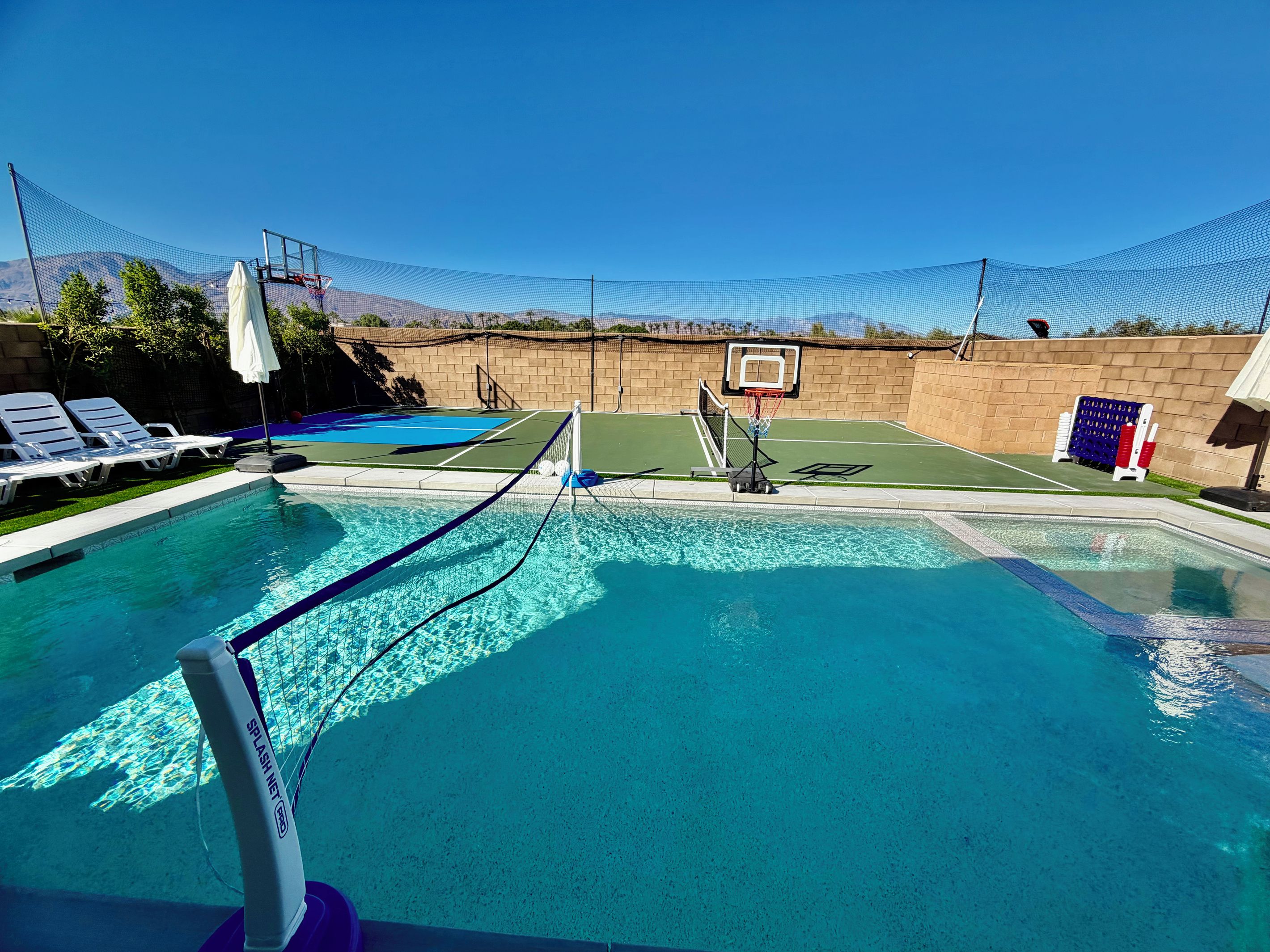 A swimming pool with a basketball hoop and a tennis net.