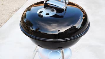 Een zwarte barbecue met deksel, wielen en handvat op een betonnen ondergrond.