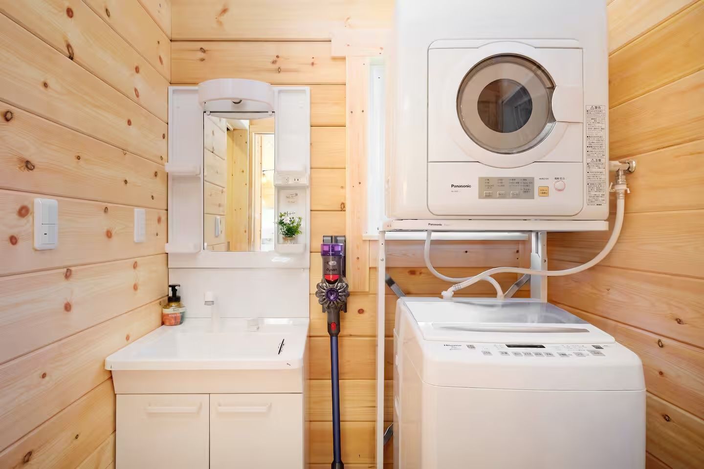 A compact, wooden-paneled bathroom with a washing machine, a dryer, and a hand dryer.