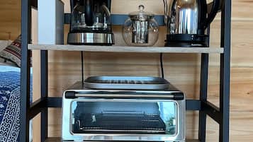 Une cuisine équipée d’un four à grille-pain encastré, d’une machine à café, d’une bouilloire et d’un petit réfrigérateur, le tout placé sur une étagère en bois.