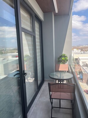 A balcony with a glass door, a small table, a chair, and a potted plant. - New Listing (Tijuana)