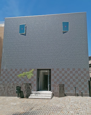 Ein Gebäude mit einem gemusterten Fassade, eine Treppe, die zu einem Eingang führt, und ein kleiner Baum neben den Stufen.