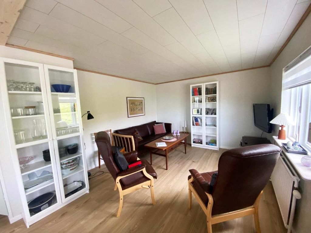 Un salon comprenant un canapé, deux fauteuils, une table basse, un meuble contenant de la verrerie et un téléviseur.