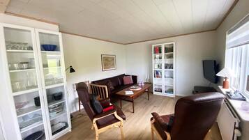 Un salon comprenant un canapé, deux fauteuils, une table basse, un meuble contenant de la verrerie et un téléviseur.