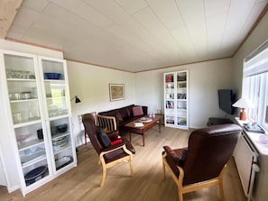 Un salon comprenant un canapé, deux fauteuils, une table basse, un meuble contenant de la verrerie et un téléviseur.
