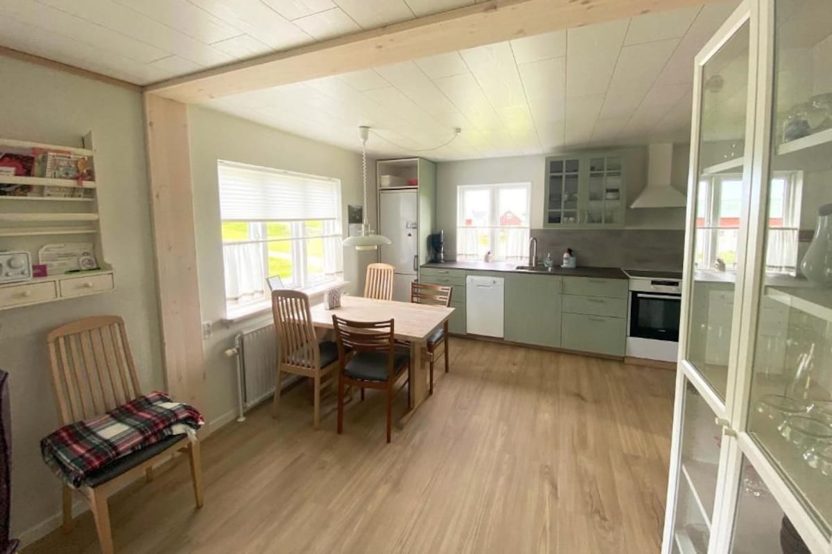 Une cuisine spacieuse avec un coin repas, un plancher en bois et une vue sur l’ext érieur grâce à une porte vitrée.