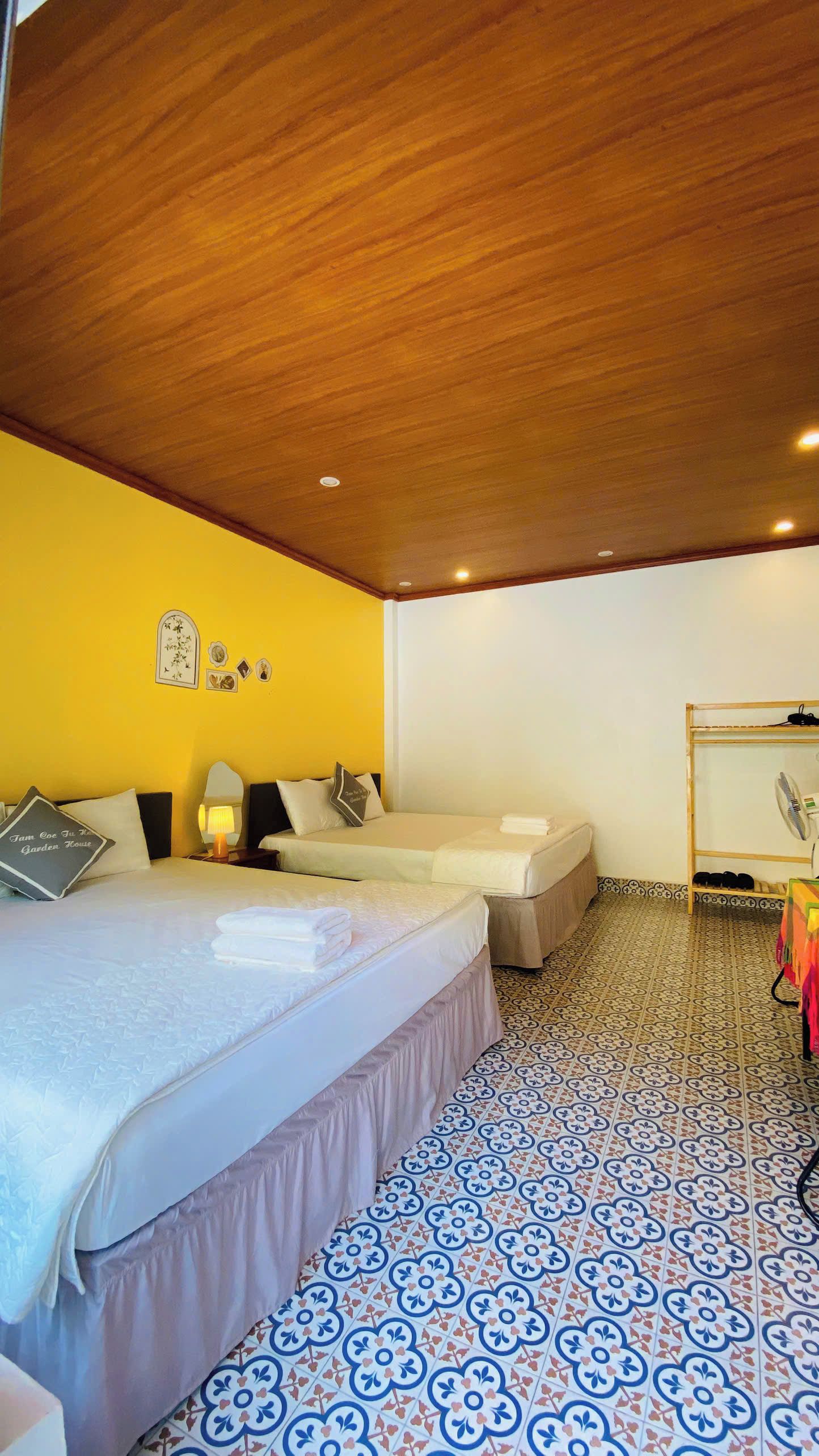 A hotel room with two beds, a wooden ceiling, and patterned floor tiles.