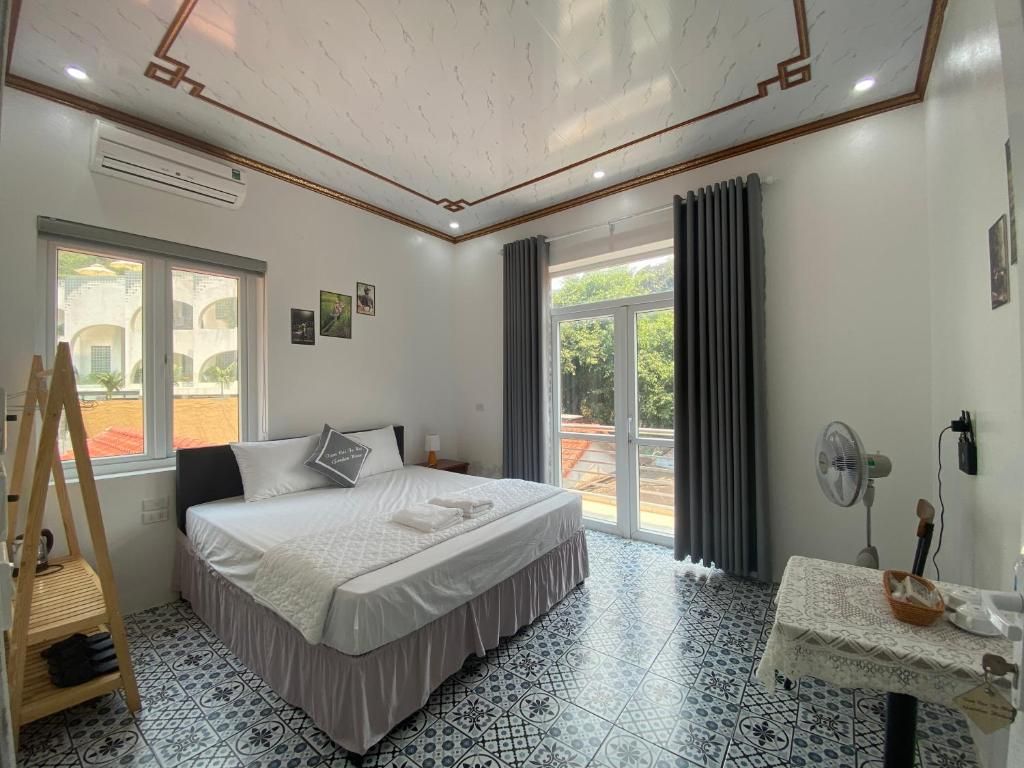 Une chambre d’hôtel avec un lit, un ventilateur, une table avec un panier, et une fenêtre avec des rideaux.