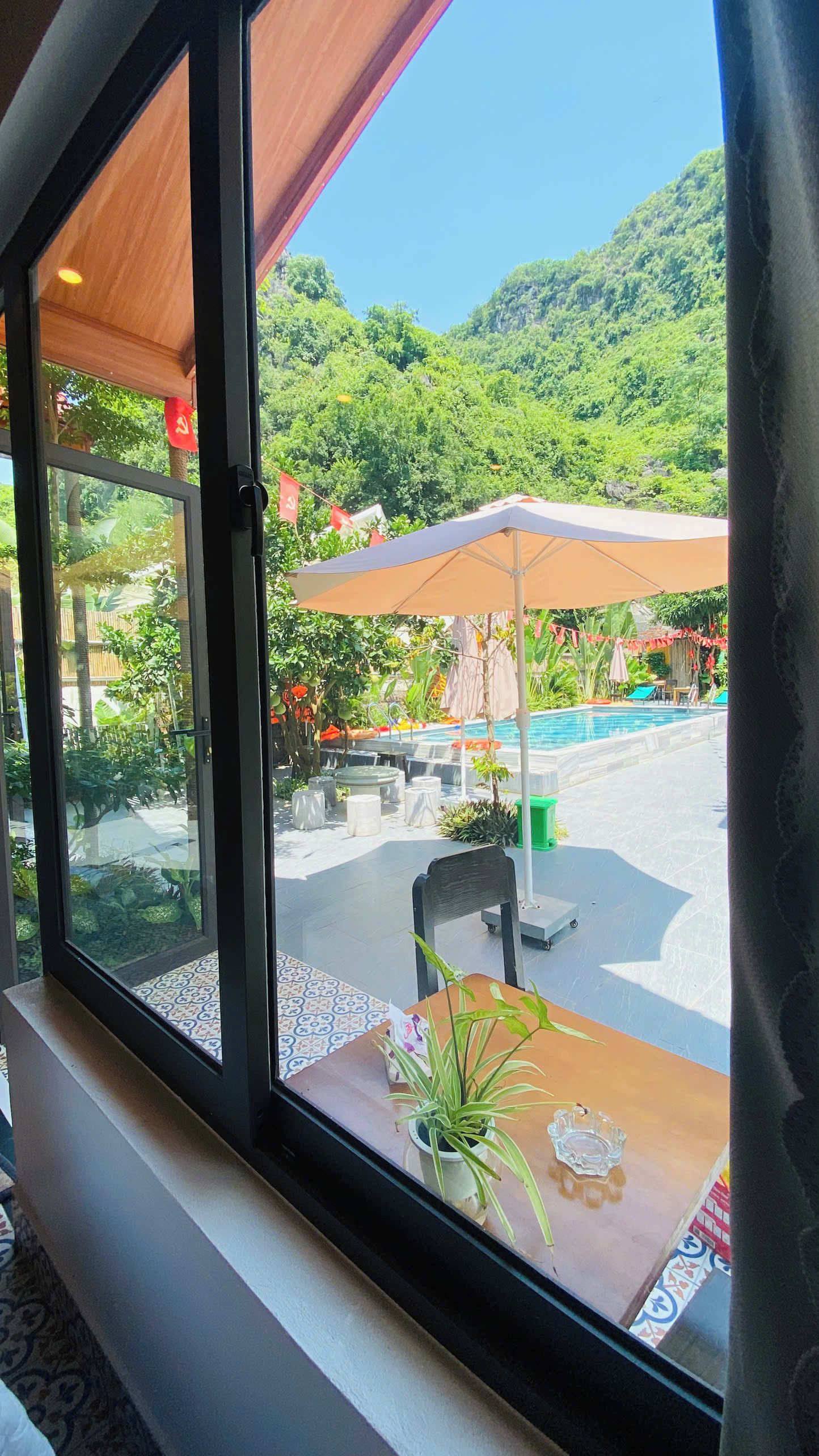 A window view of a pool area with outdoor seating and a mountain backdrop.
