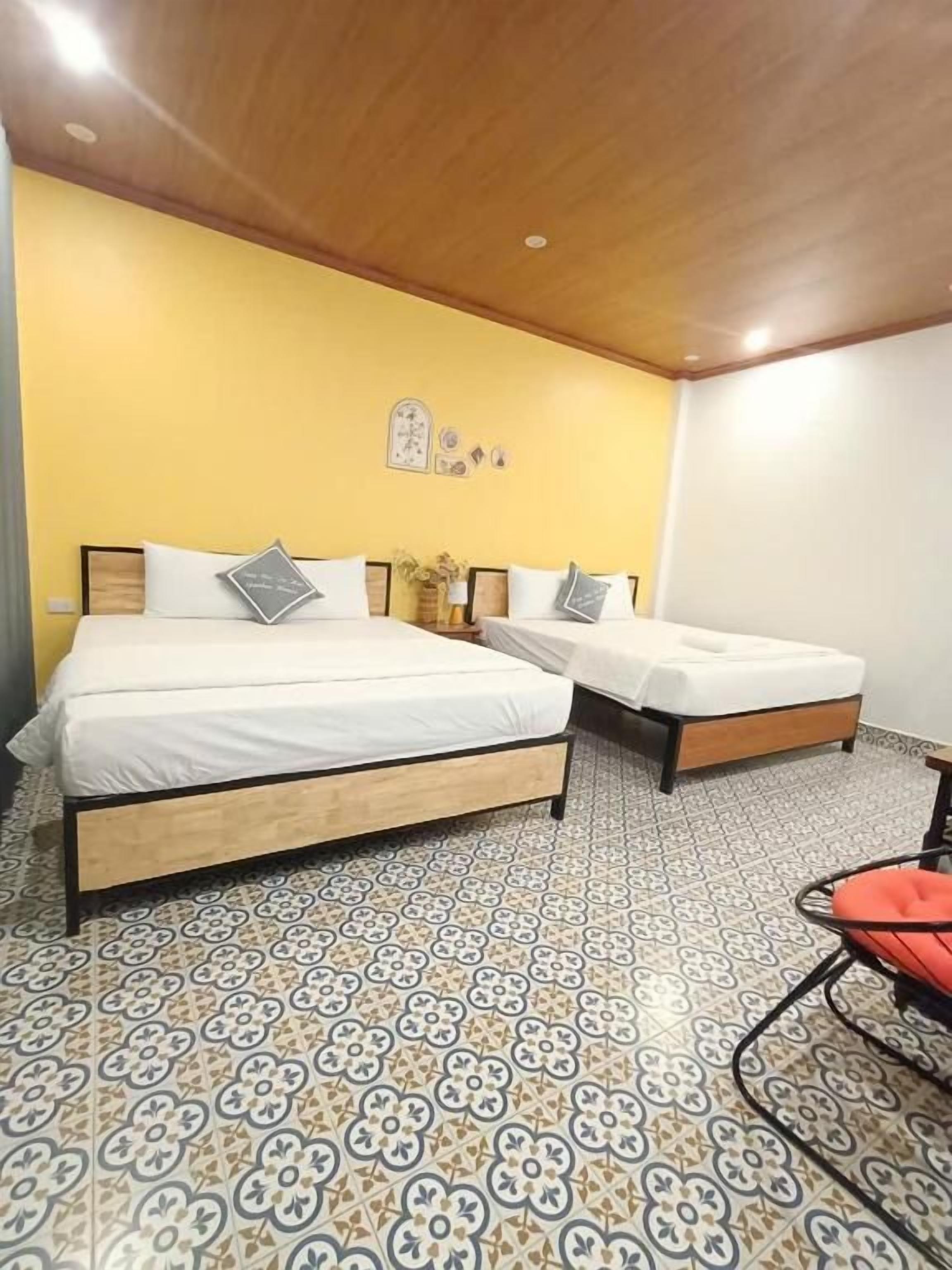 A room with two beds, a wooden ceiling, patterned floor tiles, and a chair.