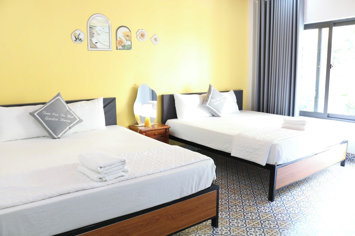 Two beds with white linens, a bedside table with a lamp, and a window with curtains.