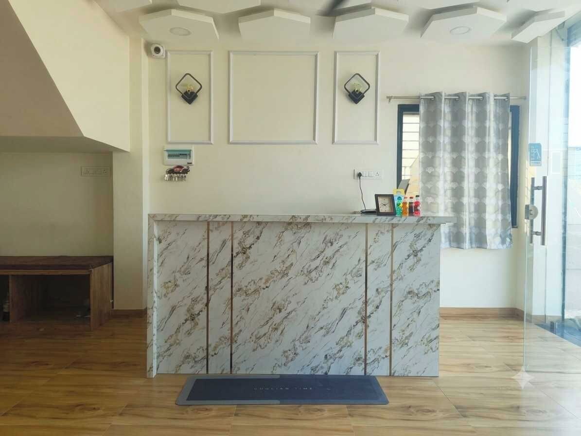 A reception desk with a marble top, a small table with items, and a bench in a room with wooden flooring and a high ceiling.