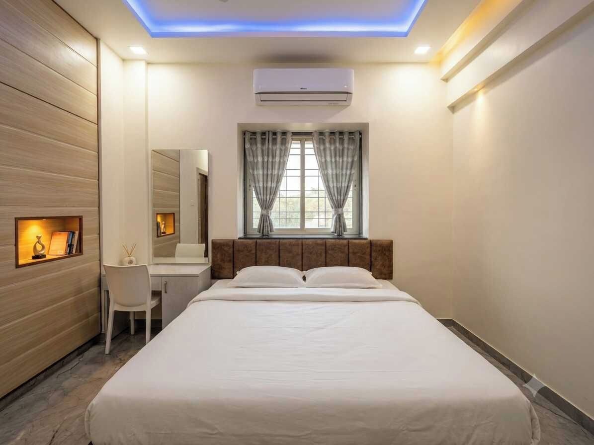 A hotel room with a bed, a desk, a chair, a mirror, and a window with curtains.