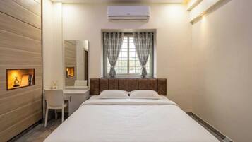 A hotel room with a bed, a desk, a chair, a mirror, and a window with curtains.