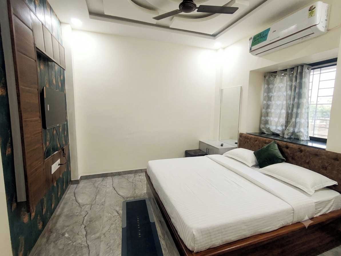 A bedroom with a bed, a ceiling fan, an air conditioning unit, a window with curtains, and a wall-mounted TV.