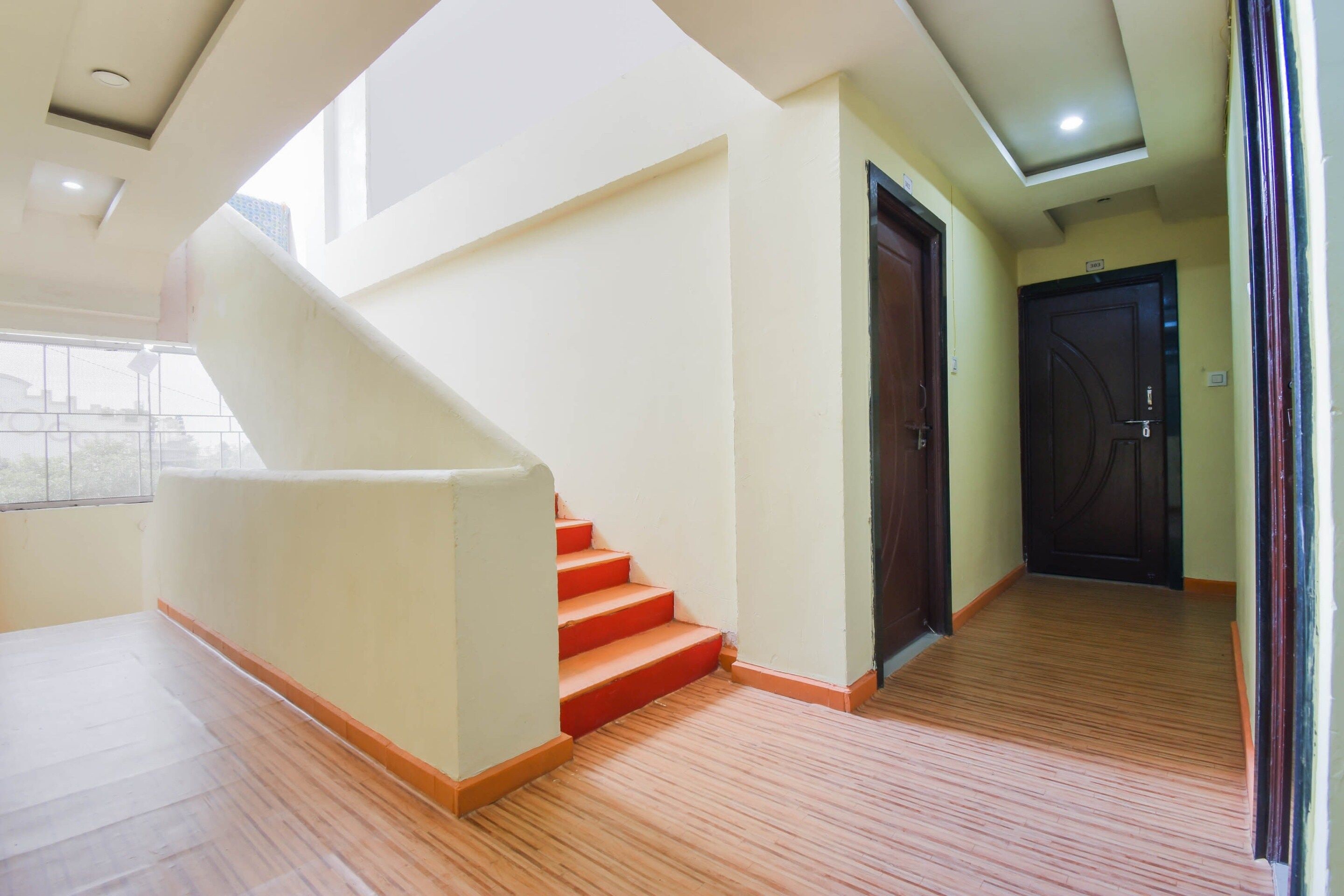 A staircase with red steps leading to a landing, a wooden floor, and a door with a number plate.
