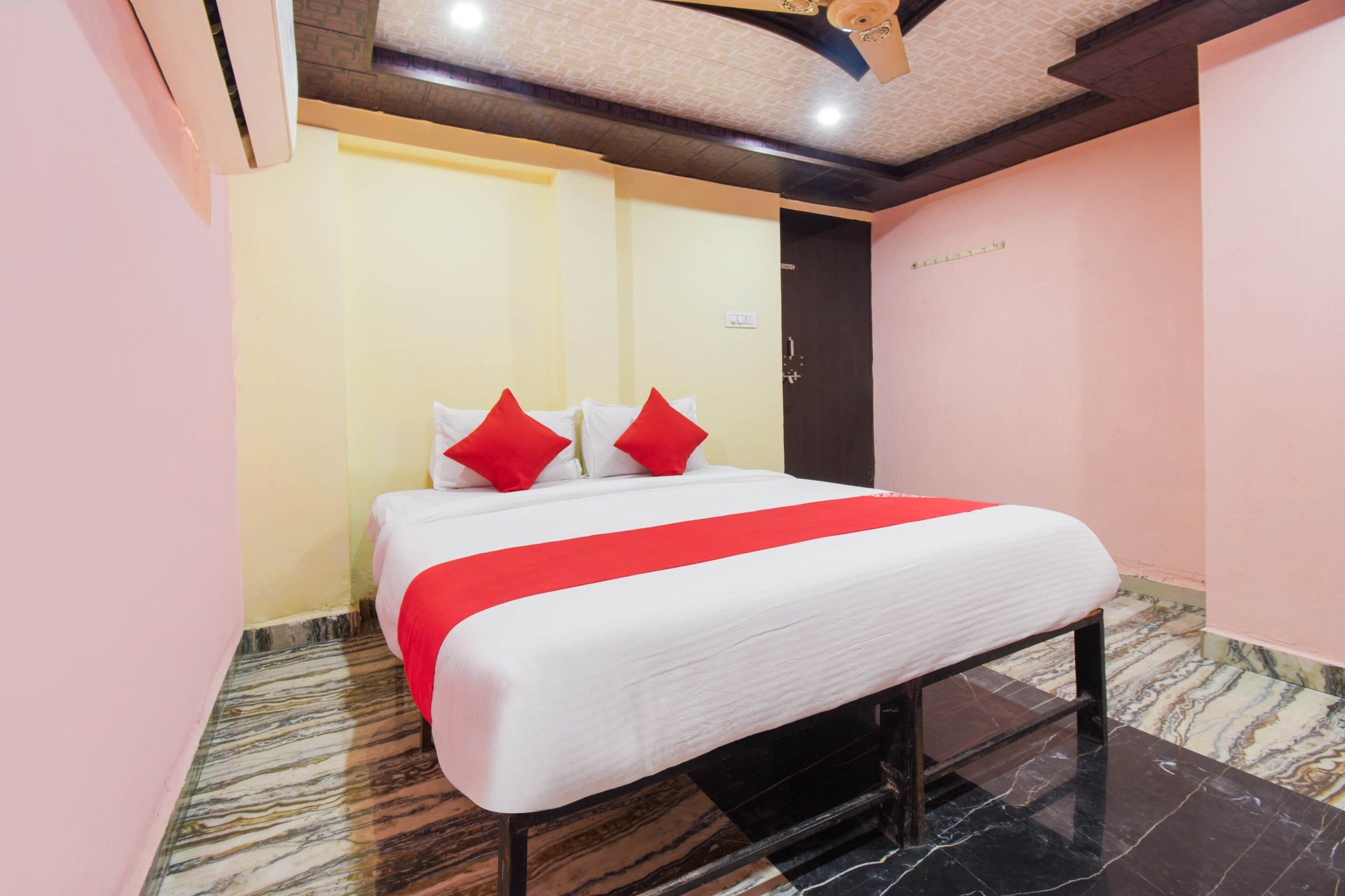Una habitación de hotel con cama, cubrecama rojo y blanco, y piso de mármol.