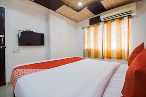 Ein Hotelzimmer mit einem Bett, einem wandmontierten Flachbildfernseher, einer Klimaanlage und einem Fenster mit gestreiften Vorhängen.