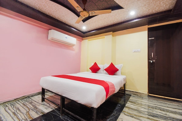 A hotel room with a bed, a ceiling fan, an air conditioning unit, and a door. - Hotel O Swastik (Nagpur)