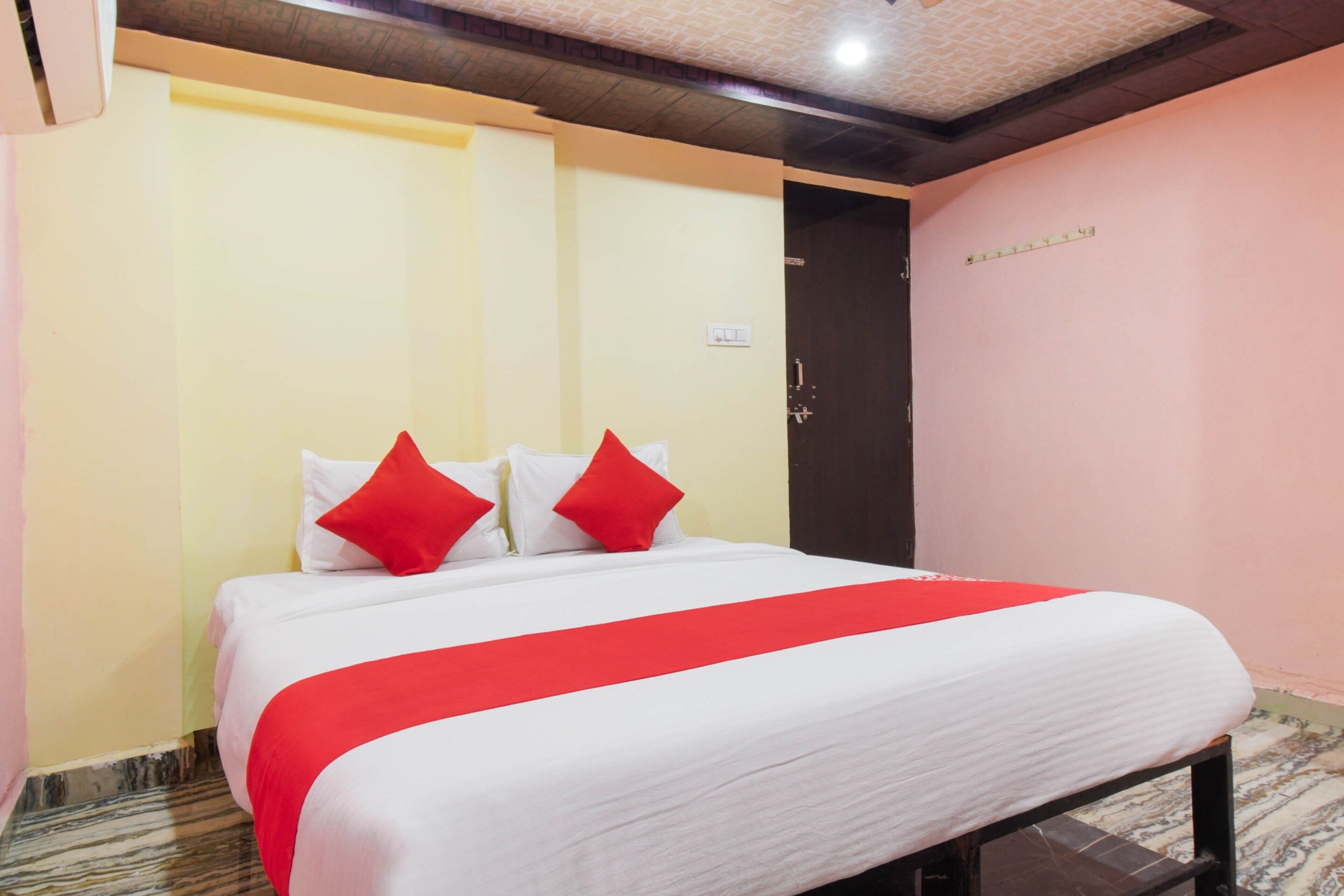 A hotel room with a bed, a door, and a wall with a light switch.