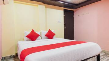 A hotel room with a bed, a door, and a wall with a light switch.