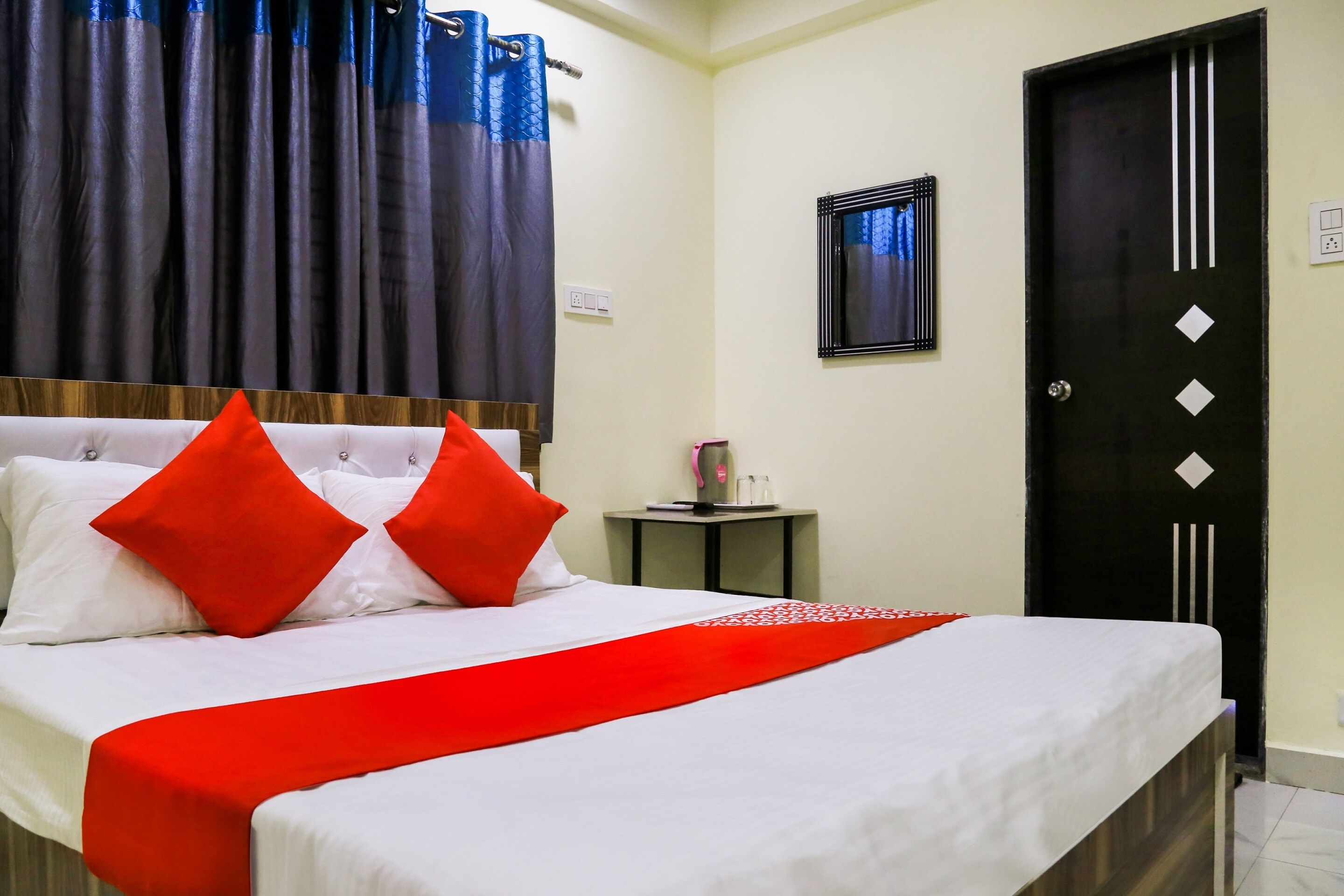 Quarto de hotel com cama, uma mesa pequena, uma porta e uma janela com cortinas.