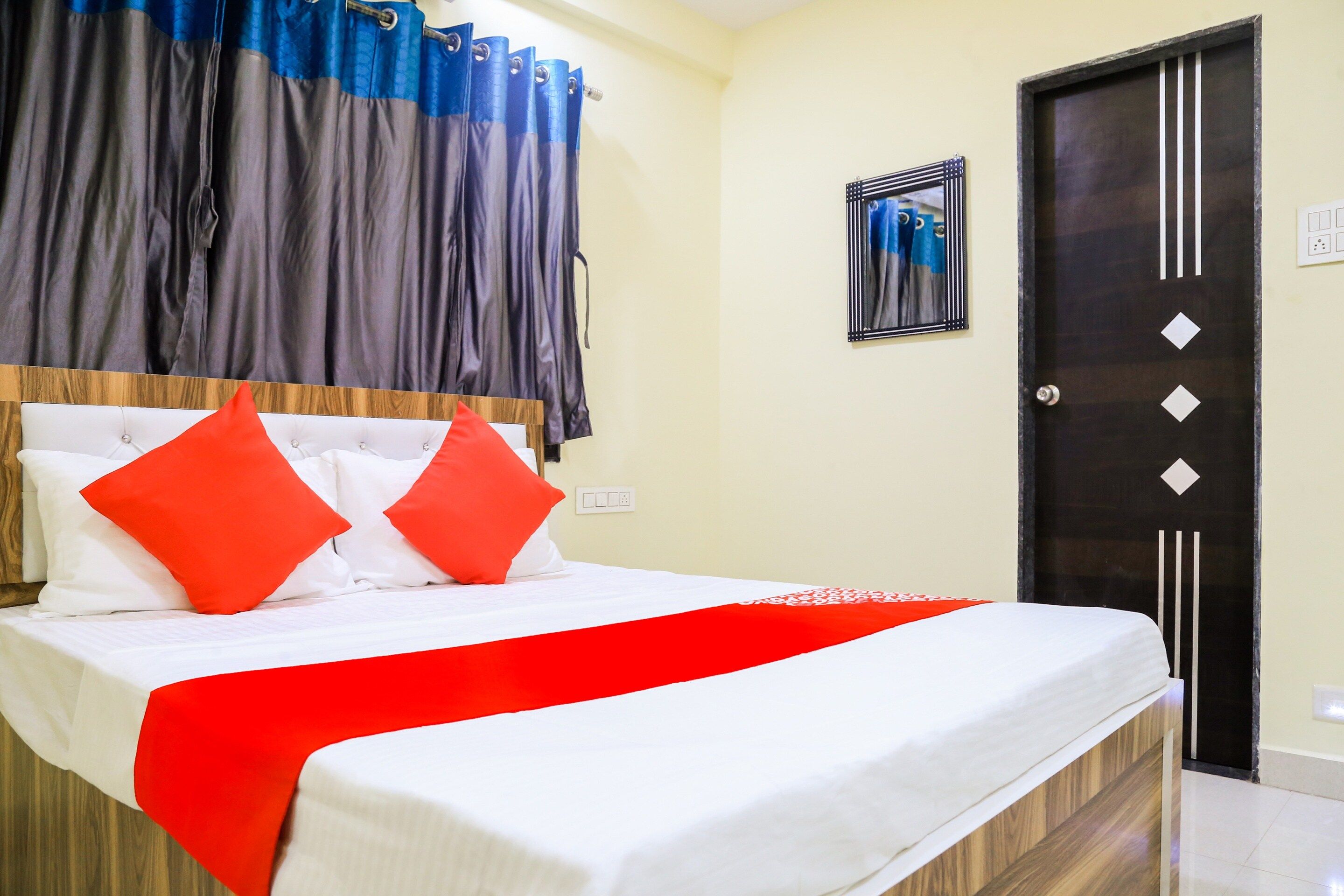 A hotel room with a bed, a red and white bedspread, and a black door.