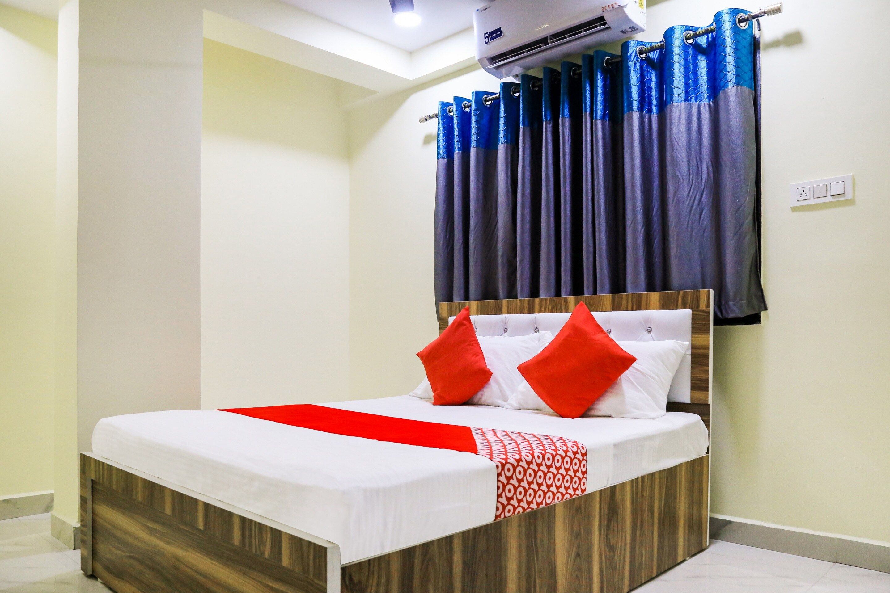 A hotel room with a bed, a red throw, and blue curtains.