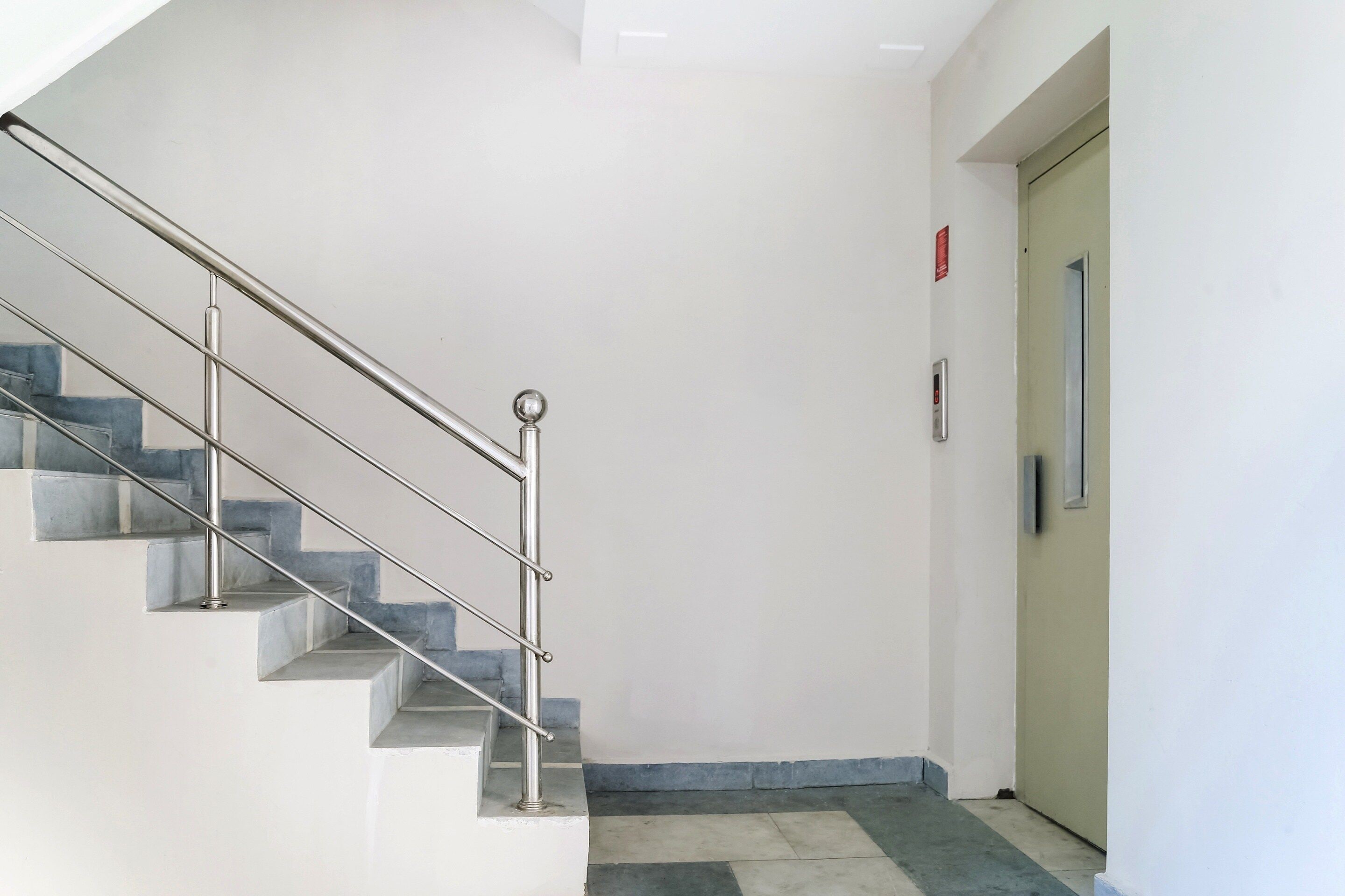 Una escalera con barandillas metálicas que conduce a una puerta con un letrero de salida de emergencia roja.
