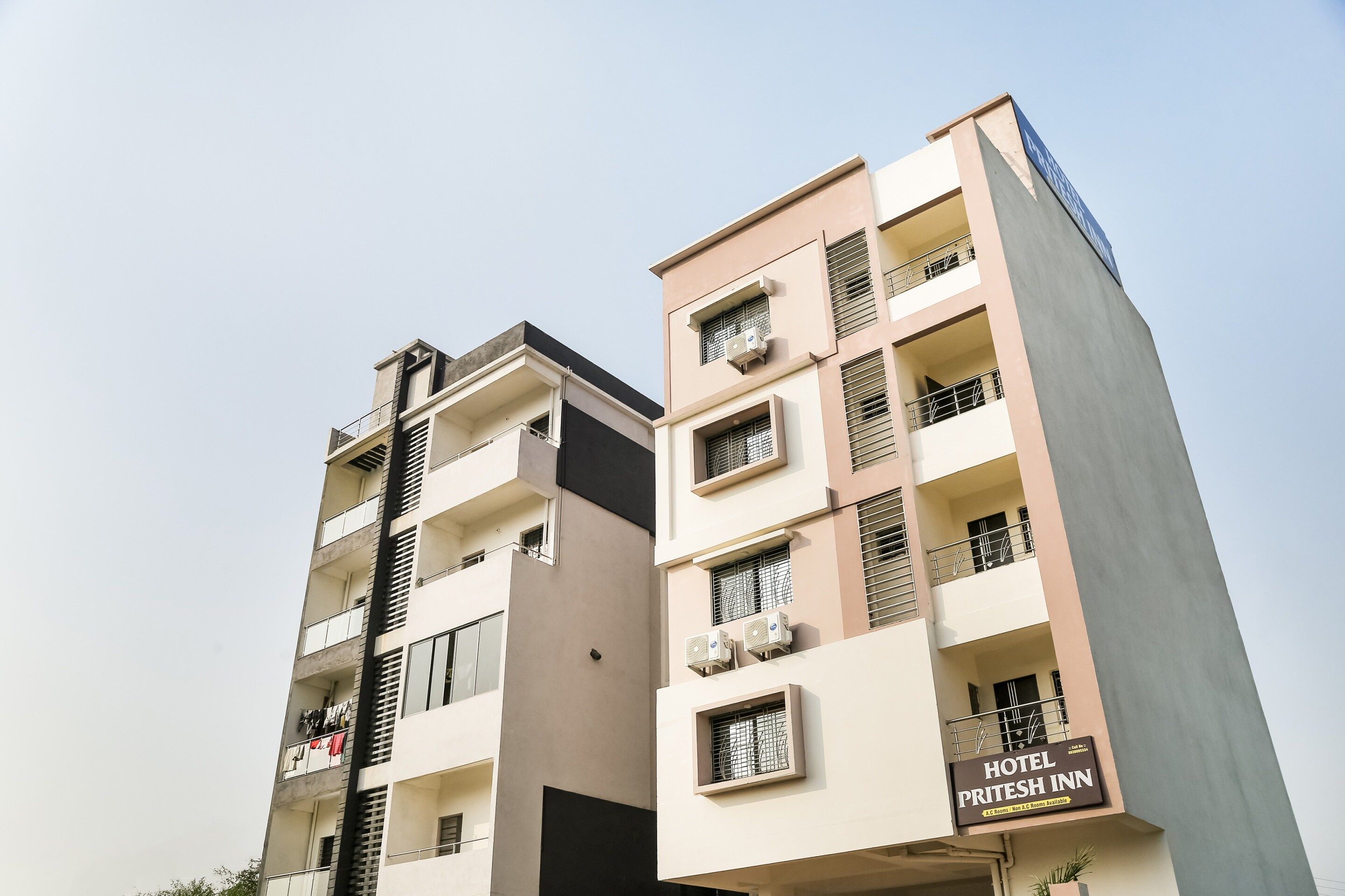 Un edificio de varios pisos con balcones, unidades de aire acondicionado y un letrero que indica que es un hotel llamado 'PRITESH INN'.